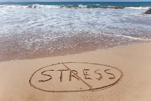 "Stress" written in sand on a beautiful beach and then crossed out to symbolize stress relief.
